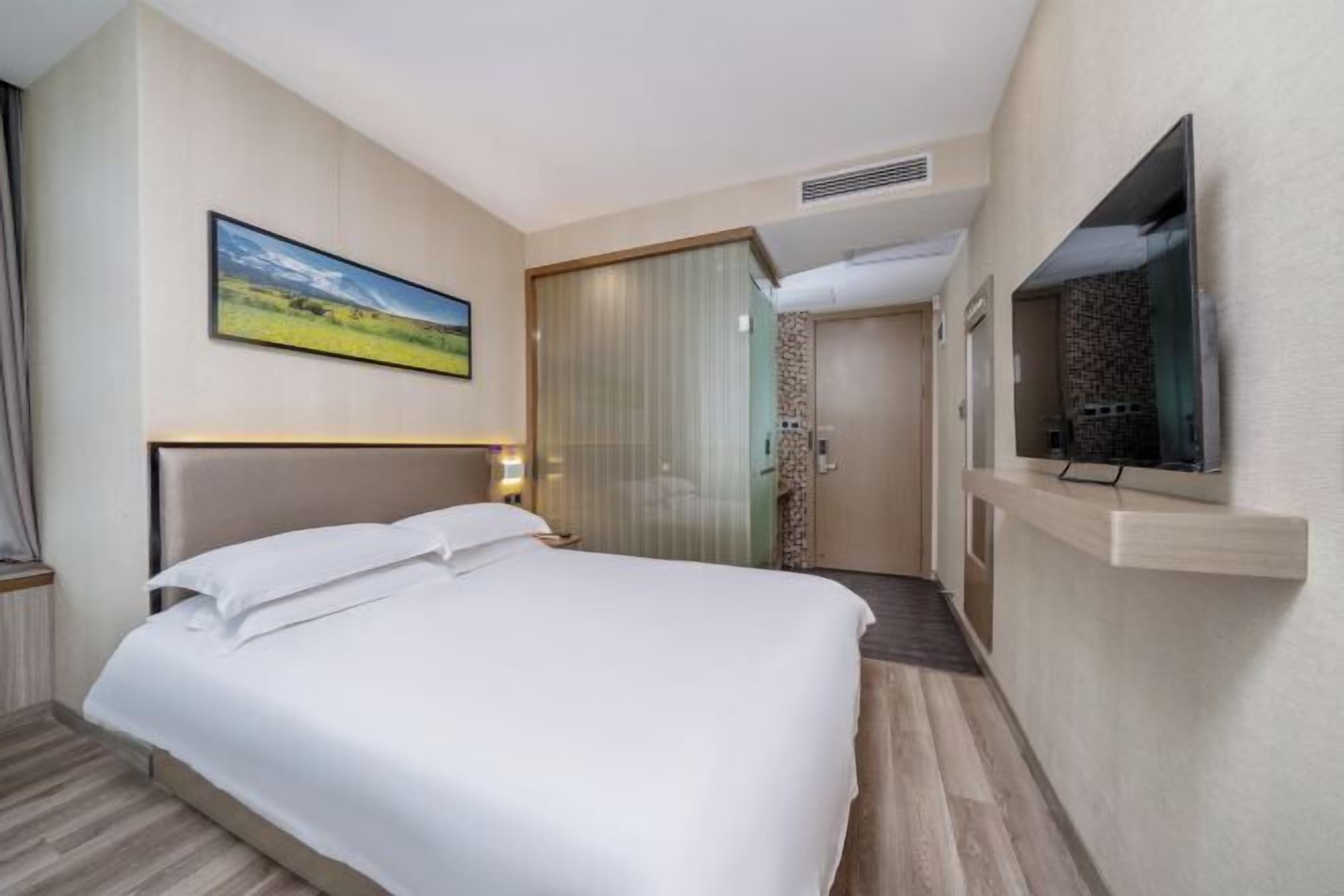 A hotel room with a bed, a television, a painting, and a door leading to a bathroom.