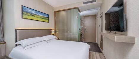 A hotel room with a bed, a television, a painting, and a door leading to a bathroom.