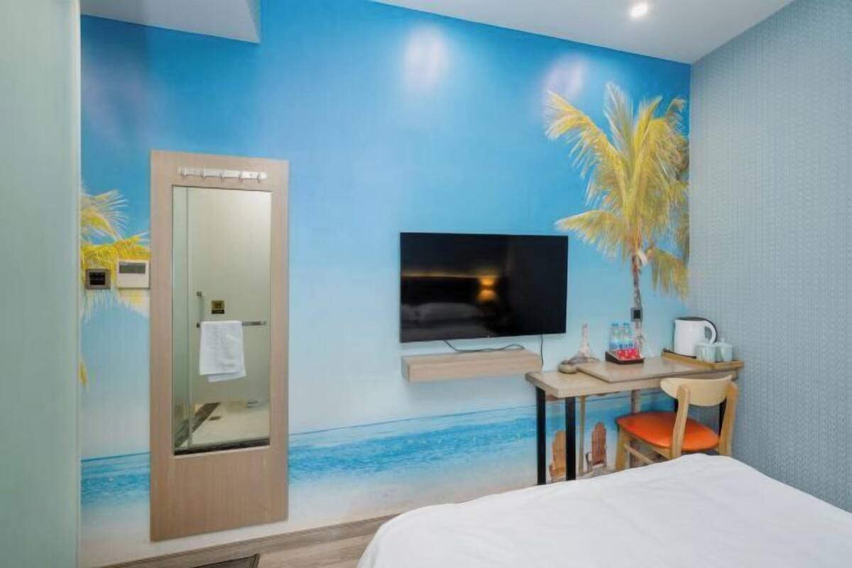 Een hotelkamer met een bed, een bureau met stoel, een televisie en een deur met spiegel.