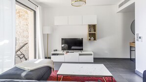 Een moderne woonkamer met een flatscreen televisie, witte meubels, een rood vloerkleed met patroon en een stenen muur.