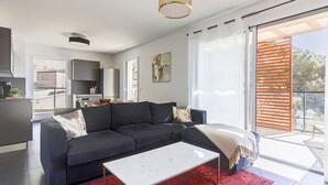 Een moderne woonkamer met een modulaire bank, een witte salontafel en een rood kleed. Achtergrond toont een keuken met kasten en een koelkast.