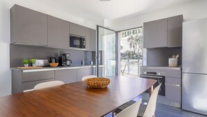 Een moderne keuken met grijze kastjes, een houten eettafel en een groot raam met uitzicht op de omgeving.
