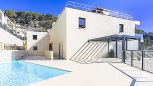 Een modern huis met een zwembad, een overdekt terras en uitzicht op de omliggende heuvels.