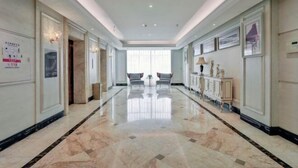 A hotel corridor with marble flooring, two chairs facing a large window, and a cabinet with decorative items. - Four Seasons Fashion Hotel (Yongkang South Railway Station Xijinqiao Pedestrian Street) (Yongkang)