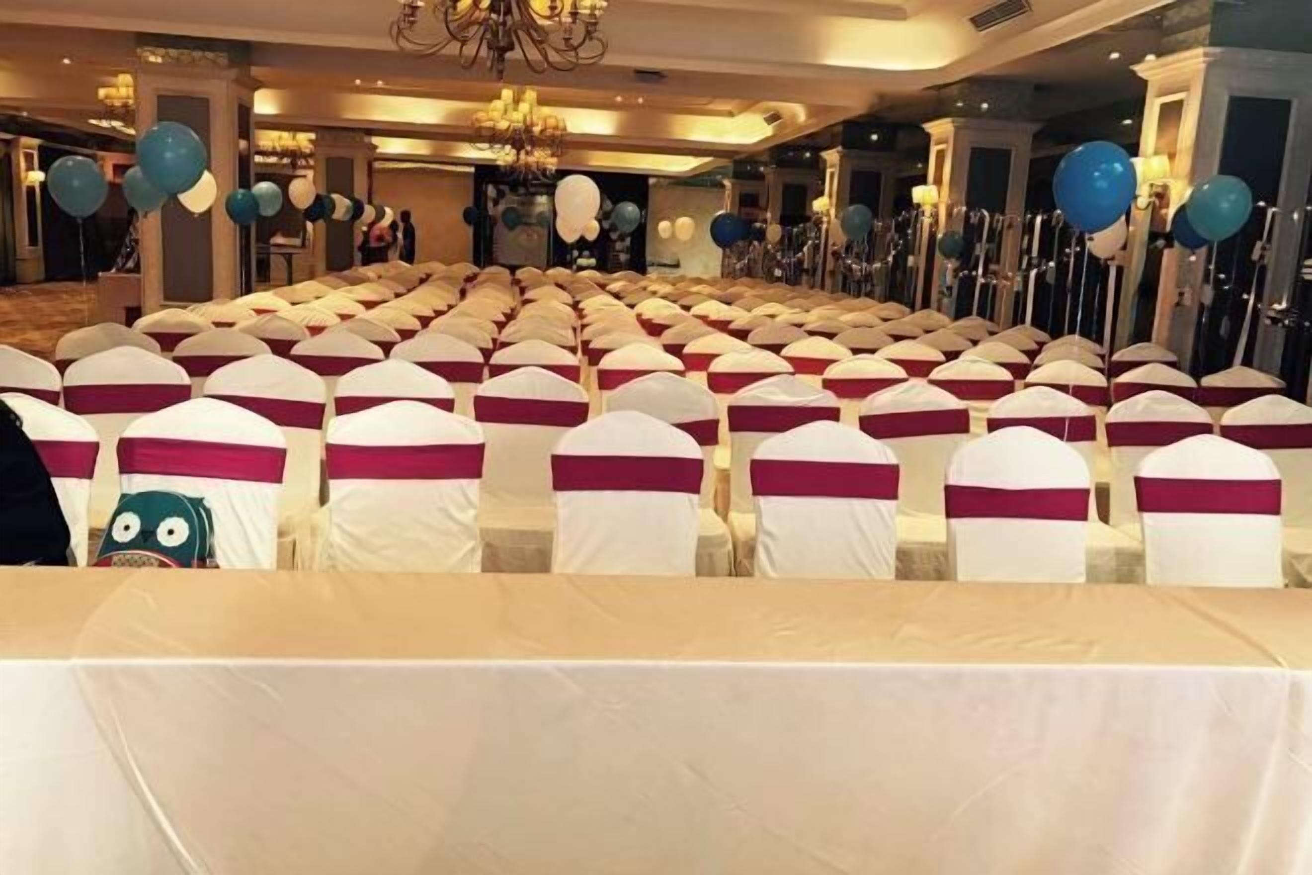 A banquet hall with rows of tables covered in white tablecloths and chairs with white and maroon sashes.