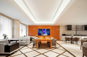 Una habitación de hotel moderna con comedor, un conjunto de sofás y un televisor montado en la pared.