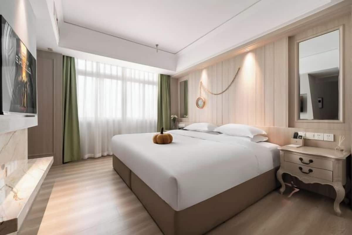 Une chambre d’hôtel moderne avec un grand lit, une table de chevet, un miroir et une fenêtre avec des rideaux.