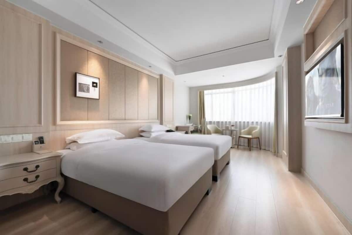 Une chambre d’hôtel moderne avec deux lits, une table de chevet, une chaise et une grande fenêtre.