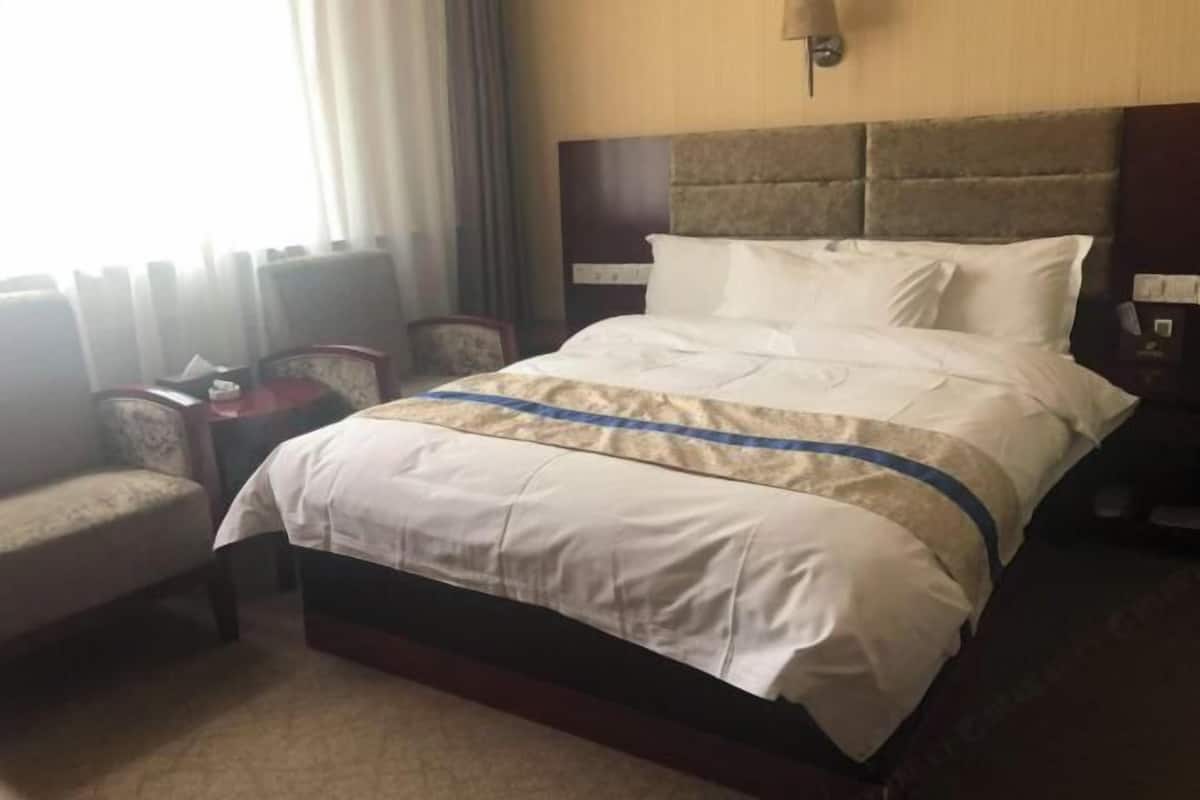 Una habitación de hotel con una cama grande, una silla, una mesita de noche y una lámpara.
