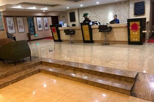 Zona de recepción de un hotel, con mostrador, sillas y una escalera que sube a un nivel superior.