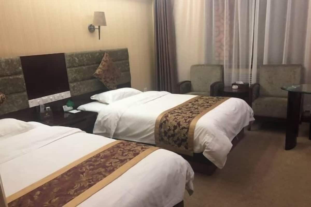 Habitación de hotel con dos camas, un escritorio, una silla, una lámpara y una ventana con cortinas.