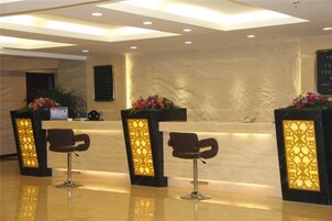 Una zona de recepción con mostrador de mármol, dos taburetes de bar y plantas decorativas.