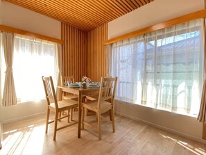 Enjoy meals in this cozy dining area with a wooden table and matching chairs, surrounded by large windows and a sloped ceiling.