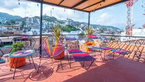 Eine Dachterrasse mit bunten Sitzgelegenheiten, Blumentöpfen und Blick auf eine Stadtlandschaft.