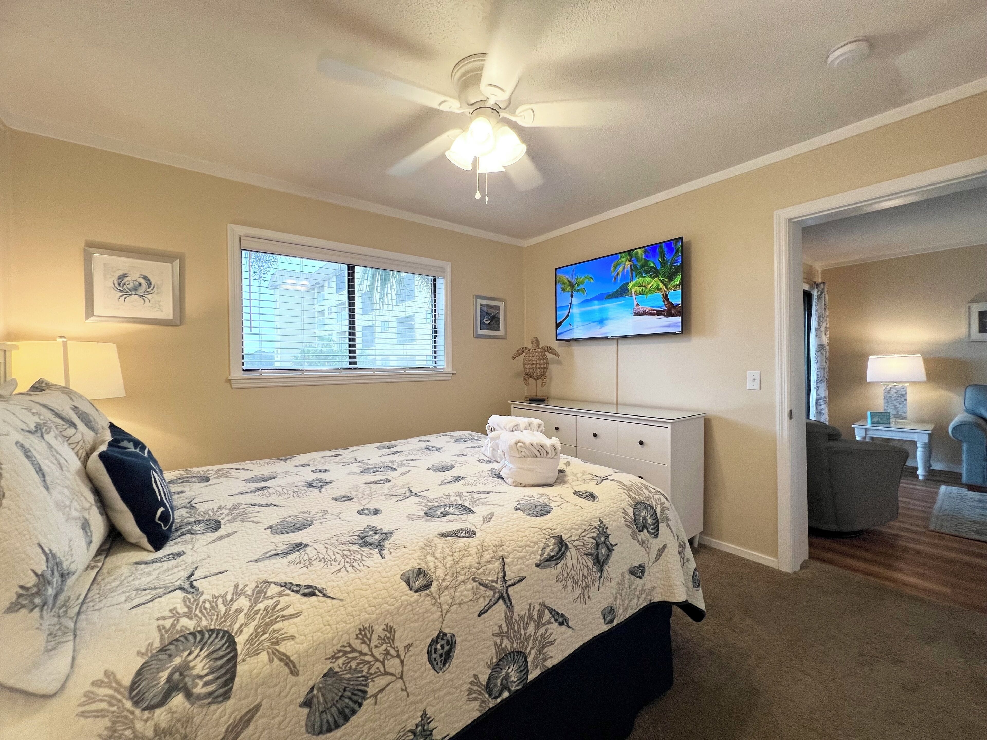 Ein Schlafzimmer mit einem Bett, einem Deckenventilator, einem Fernseher und einem Fenster mit Jalousien.