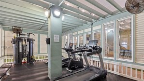 Une salle de sport équipée de tapis de course, d’une machine de musculation et d’un ventilateur.