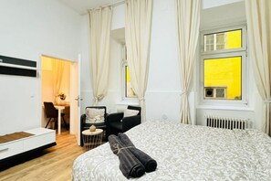 Ein Schlafzimmer mit Bett, Schreibtisch, Stuhl und einem Fenster mit Vorhängen.