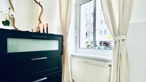 Une pièce avec une commode noire, une fenêtre avec des rideaux et un radiateur.