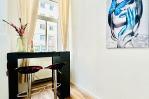Una habitación con chimenea de marco negro, dos taburetes de bar, un jarrón con flores y un cuadro grande en la pared.