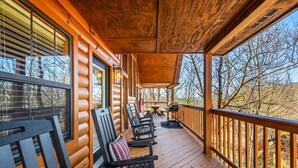 Eine Holzterrasse mit mehreren Stühlen und einem Tisch, mit Blick auf ein bewaldetes Gebiet.