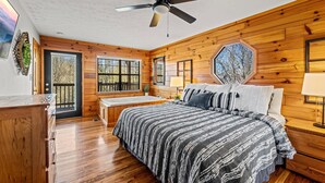 Ein Schlafzimmer mit einem großen Bett, einem Deckenventilator, Holzwänden, einem Fenster und einer Tür.