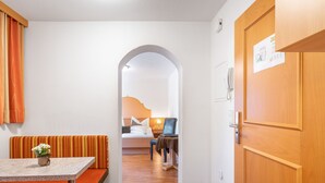 A hotel room with a kitchenette, a dining area with a bench, a bed with a nightstand, and a bathroom visible through an archway. - Apartment Rosa by Interhome (Mayrhofen)