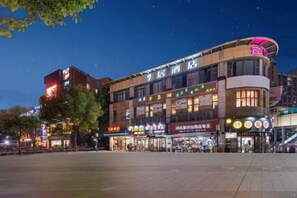 Un hôtel à plusieurs étages, doté d’une enseigne bien visible, d’une vaste place ouverte devant et de divers commerces au rez-de-chaussée.