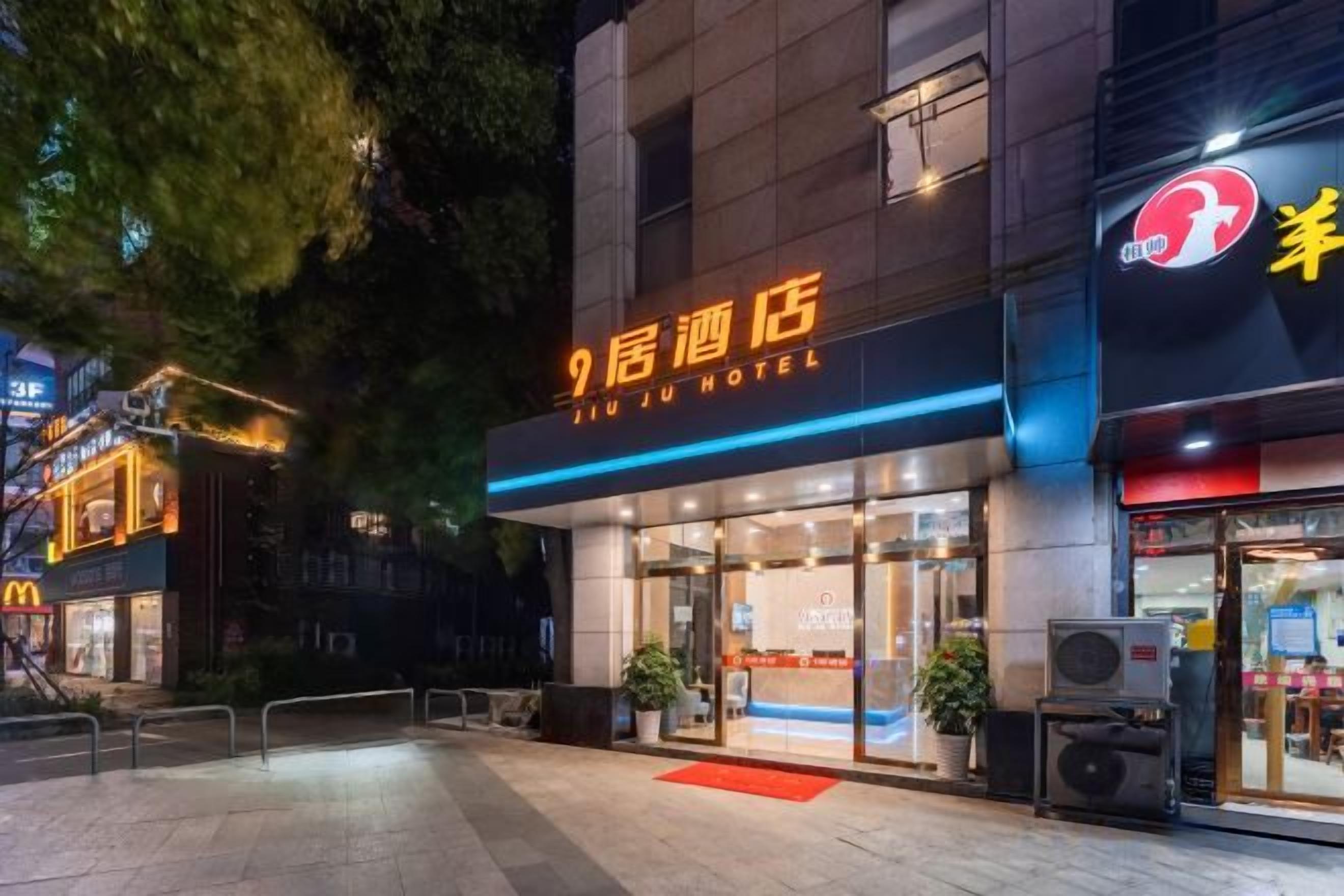 A hotel entrance with a sign reading '9th Hotel,' a glass facade, and a red carpet leading to the door.