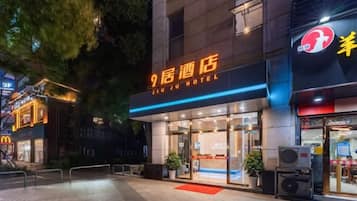 A hotel entrance with a sign reading '9th Hotel,' a glass facade, and a red carpet leading to the door.