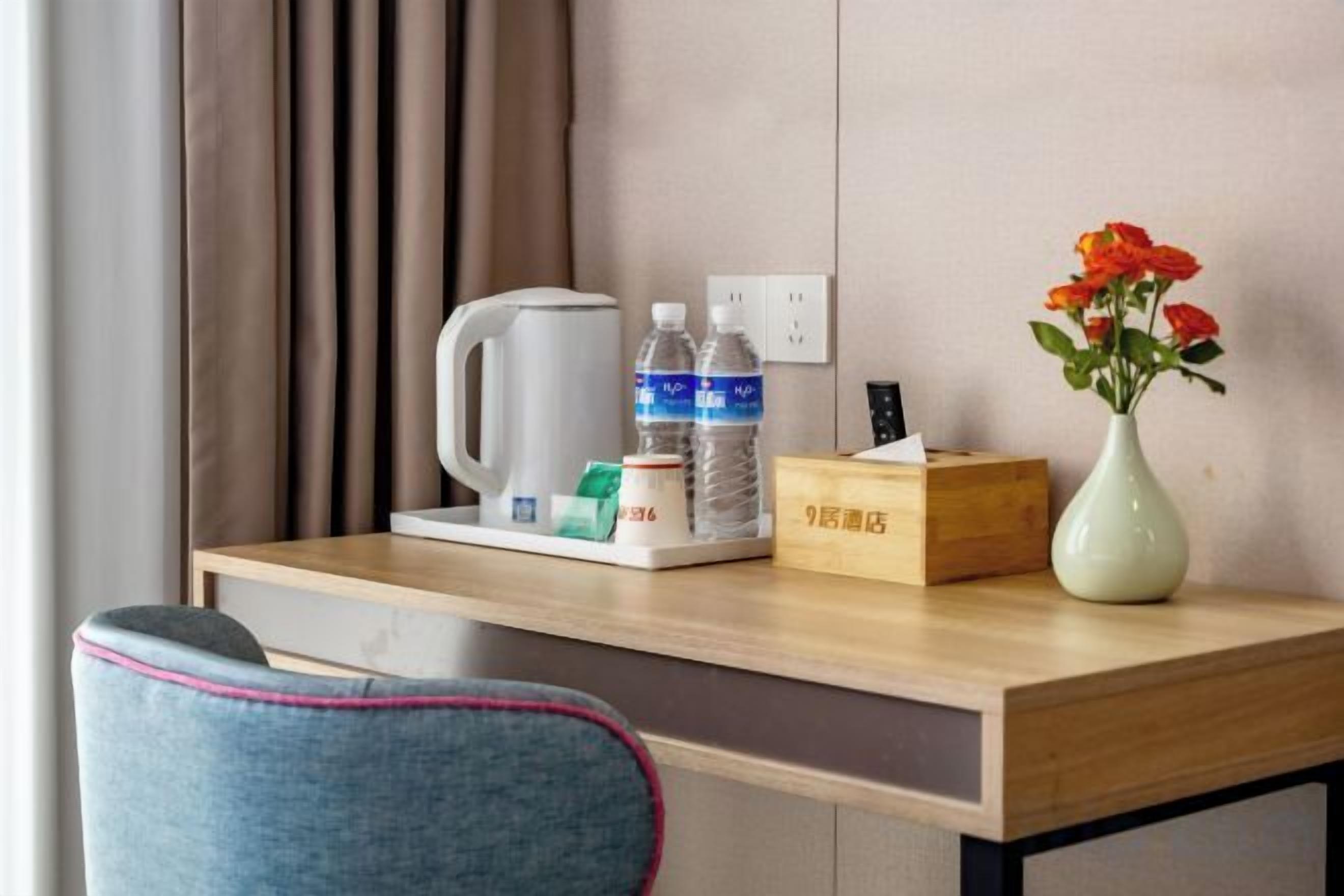 Escritorio de habitación de hotel con cafetera, botellas de agua, caja de pañuelos y un jarrón con flores.