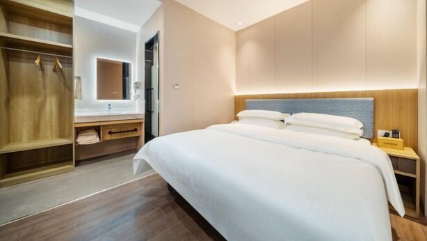 A modern hotel room with a large bed, wooden wardrobe, and a built-in vanity with a mirror. - Jiu Ju Hotel (tongnan South Road) (Shanghai)
