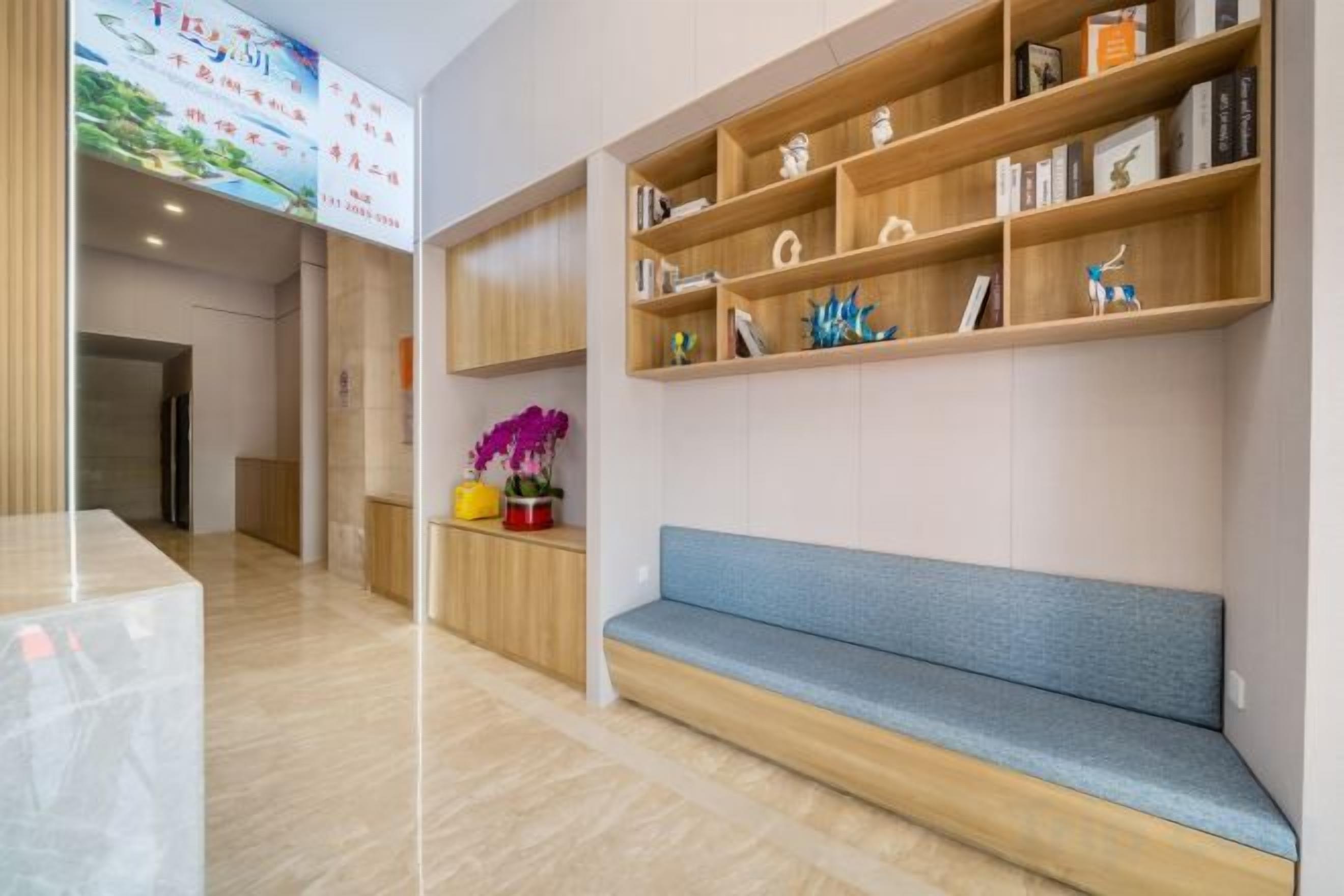 A reception area with a bench, wooden shelves with books and decorative items, and a wall-mounted TV.