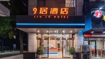 The entrance of JIU JU HOTEL with a modern facade, glass doors, and a red carpet leading to the reception area.