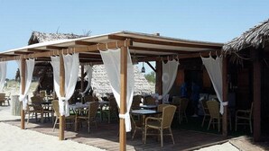 A beachside restaurant with wooden tables and chairs, covered by a wooden pergola with white curtains. - La Conchiglia  - Piscina e Animazione gratuita (Bernalda)