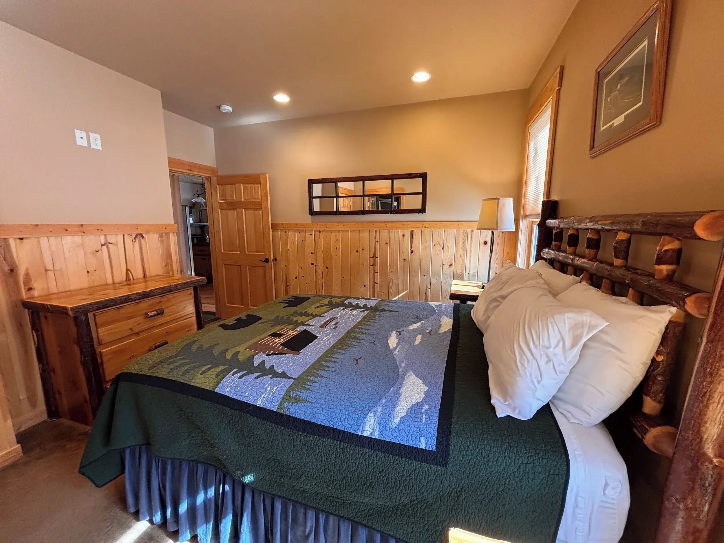 A bedroom with a bed, a wooden headboard, a nightstand, a lamp, a mirror, and a door.