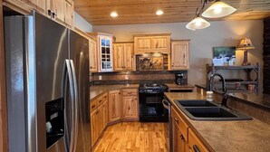 A modern kitchen with wooden cabinets, a stainless steel refrigerator, a stove, and a sink. - Lakeview Home with Dock on the Whitefish Chain, Outdoor Pool, Pickleball & More (Pequot Lakes)