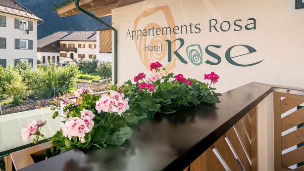 Ein Hotelzeichen mit dem Namen "Appartements Rosa Hotel Rose" und Blick auf die umliegenden Gebäude und Berge.