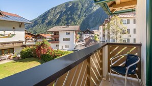 Ein Balkon mit Bergblick, einem Holenzaun und einem Stuhl.