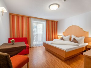 Relax in a stylish room with a large bed, a small table, and a comfortable chair, offering a view of the outside through sheer curtains.