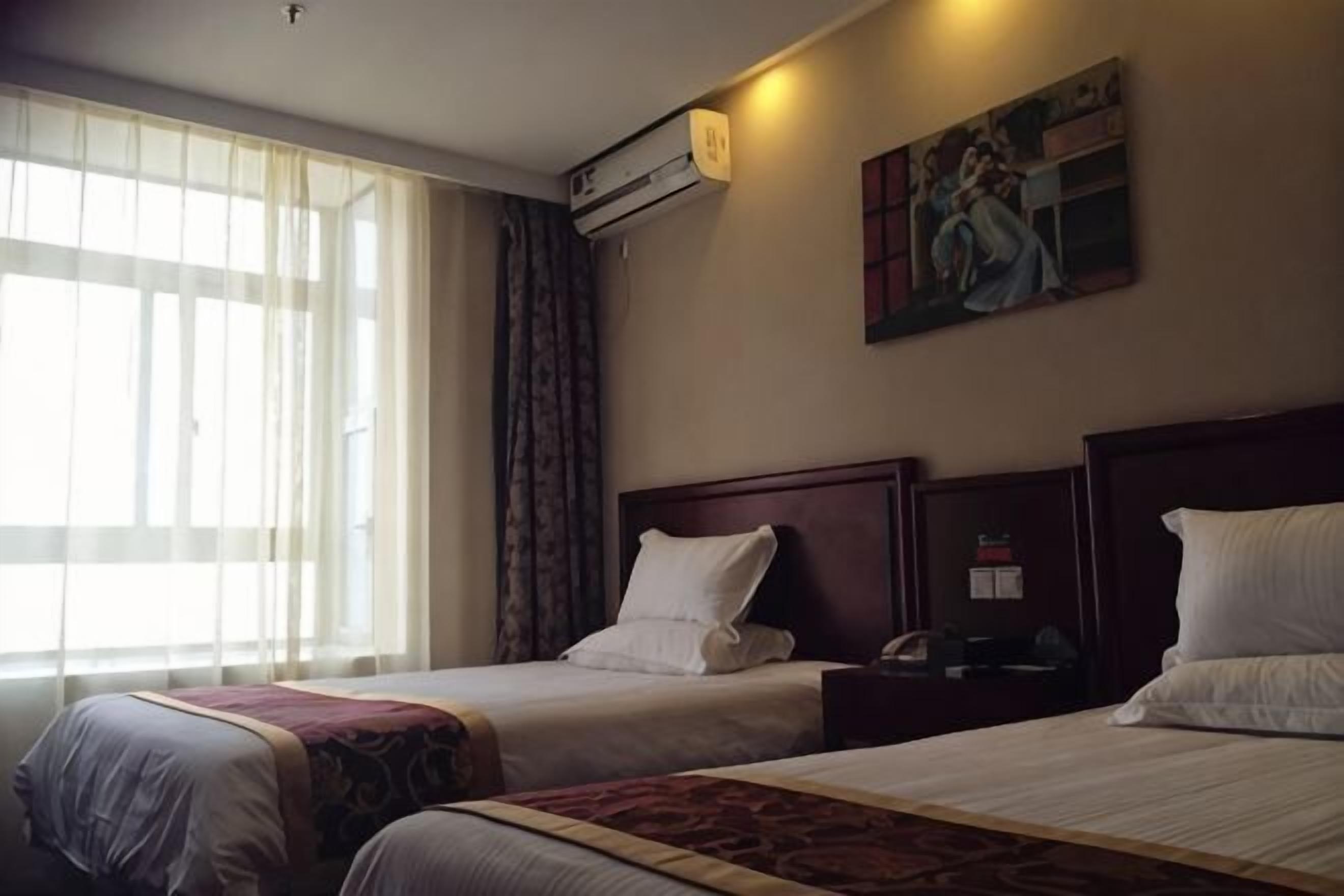 A hotel room with two beds, a painting on the wall, and a window with curtains.