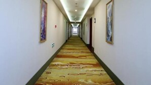 A long, narrow hotel hallway with patterned carpet, framed artwork on the walls, and a ceiling with recessed lighting. - Greentree Inn Newtown Malu Subway Station Business (Shanghai)