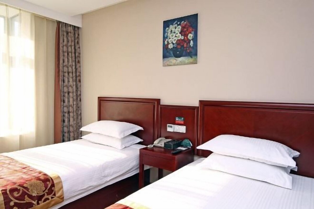 A hotel room with two beds, a nightstand with a phone, a painting on the wall, and a window with curtains.
