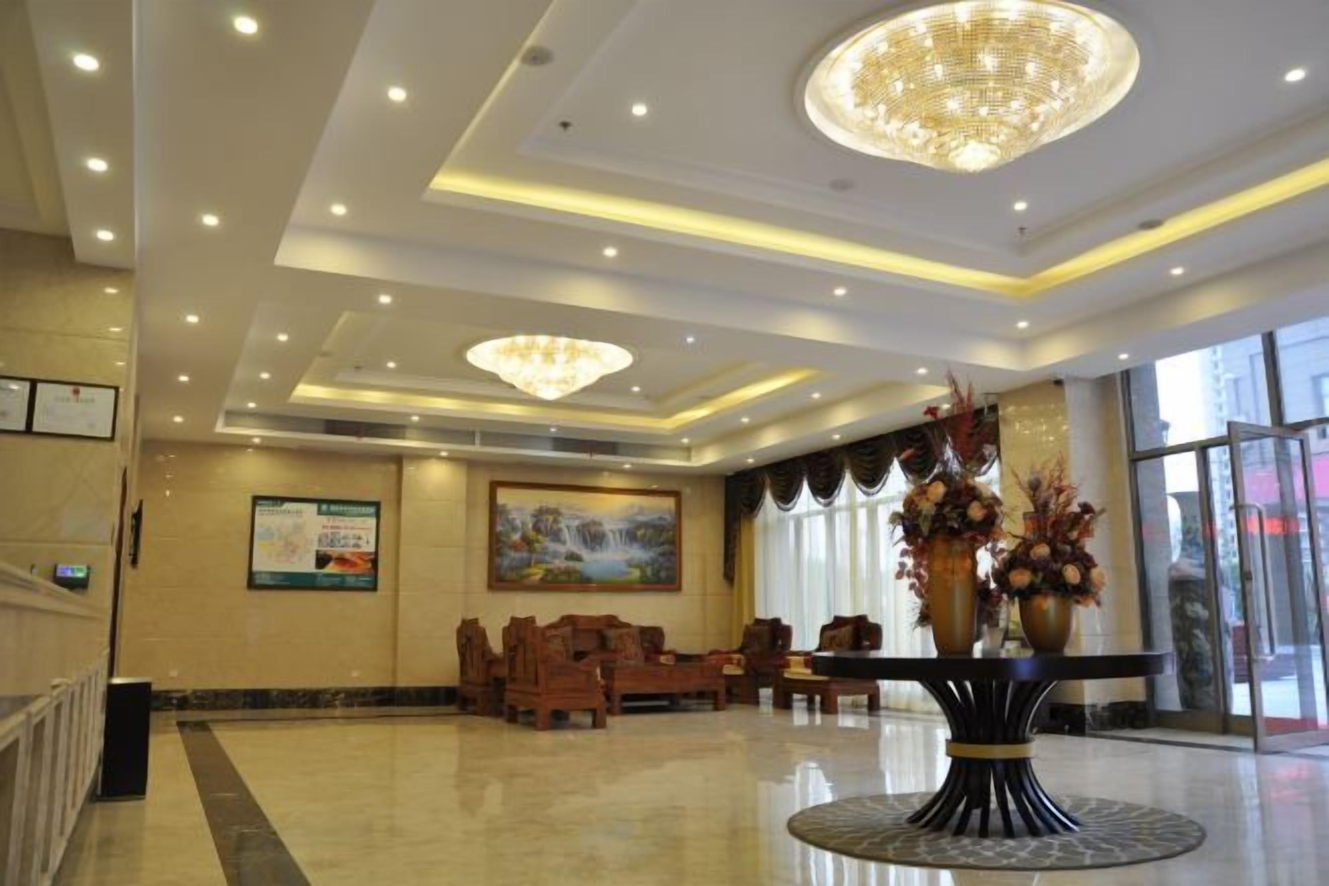 A hotel lobby with a chandelier, seating area, and a large painting on the wall.