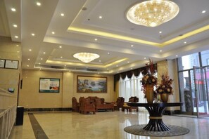 A hotel lobby with a chandelier, seating area, and a large painting on the wall.