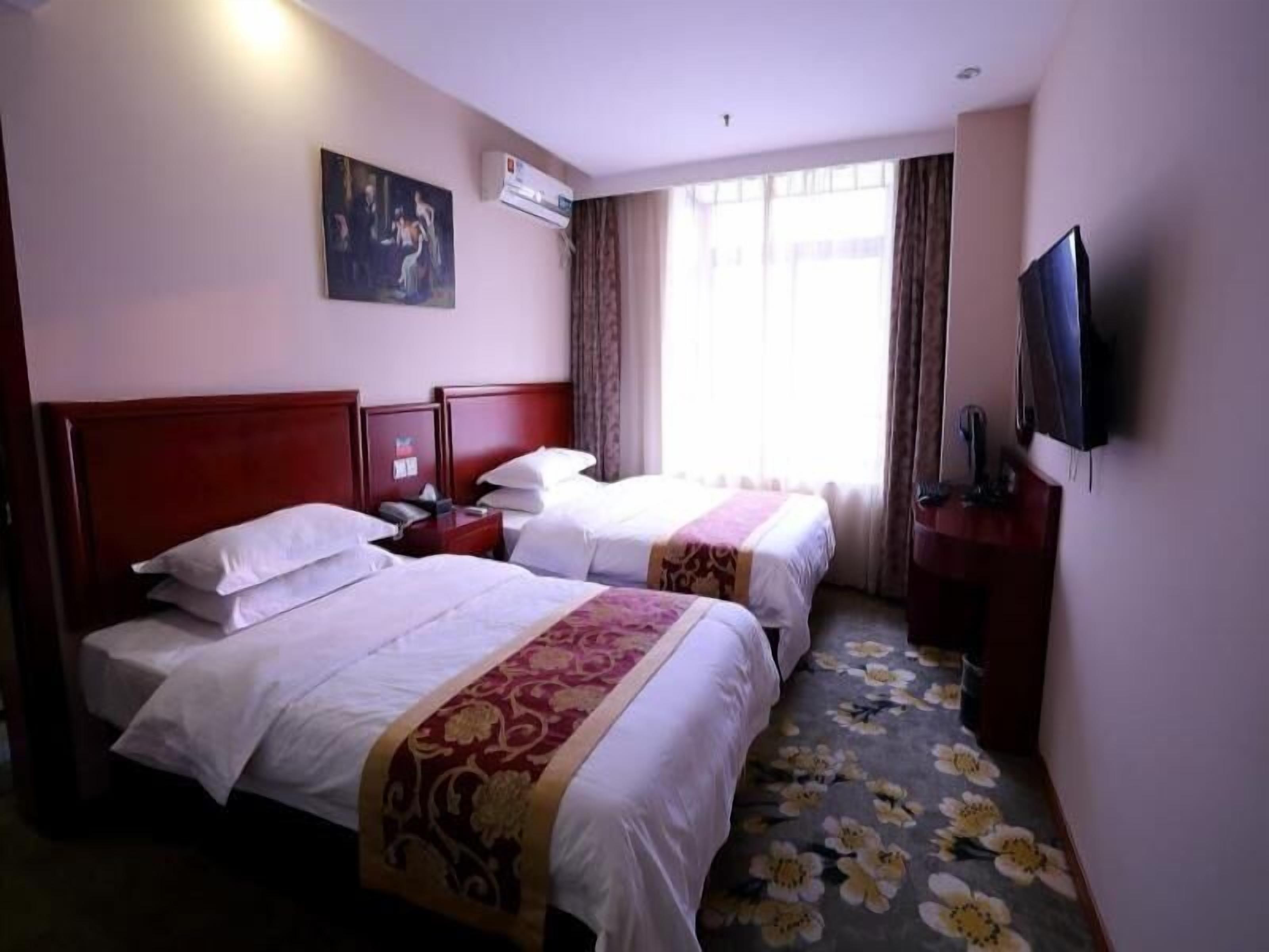 A hotel room with two beds, a television, an air conditioning unit, and a painting on the wall.