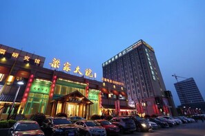 A hotel with a prominent entrance, multiple floors, and a parking lot with cars.