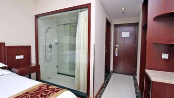 A hotel room with a bed, a shower area, and a wooden wardrobe.