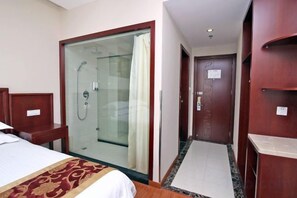 A hotel room with a bed, a shower area, and a wooden wardrobe.