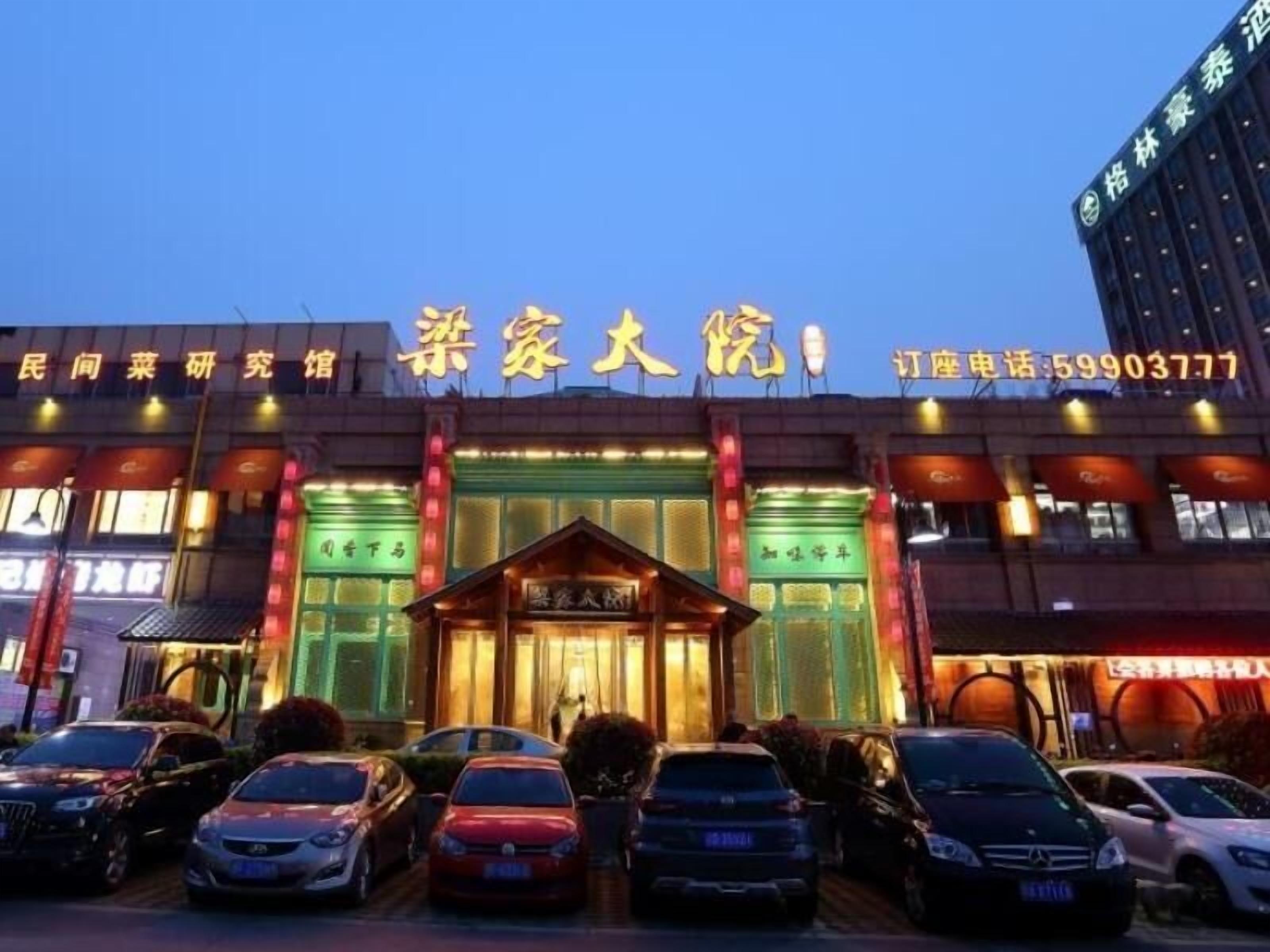 Un hotel con una entrada destacada, varios coches estacionados frente a él y señalización iluminada.