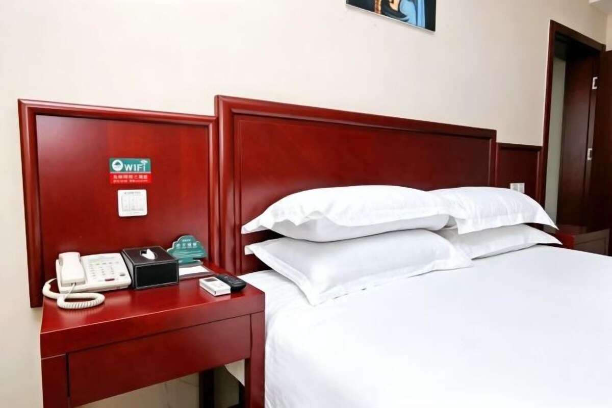 A hotel room with a wooden headboard, a bed with white linens, a bedside table with a phone, a WiFi sign, and a nightstand.